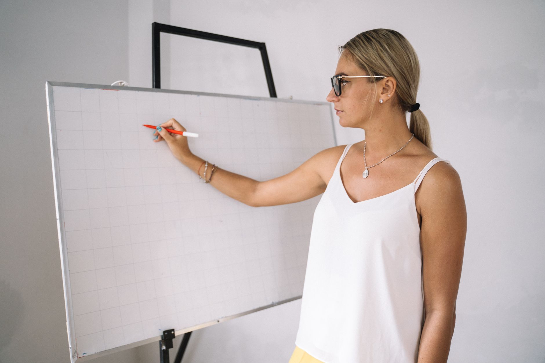 Caucasian woman with eyeglasses writing on a whiteboard during a classroom session.