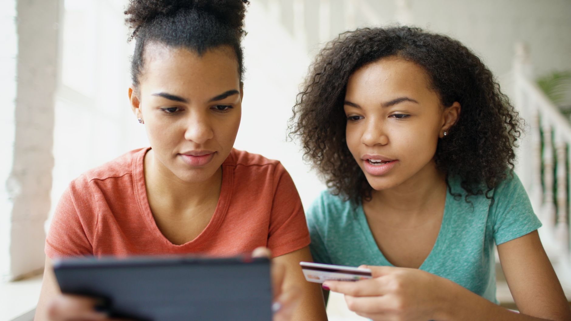 Two young women using a tablet for online shopping with a credit card.