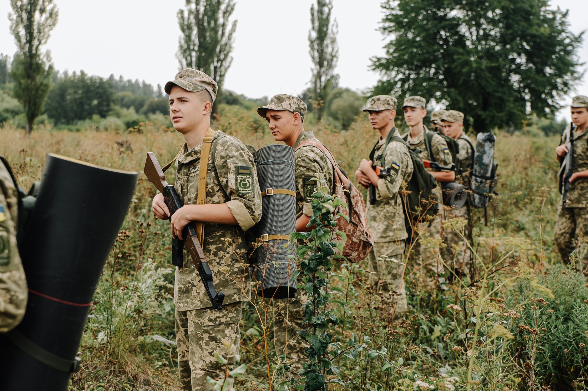 Group of soldiers in camouflage uniforms on a field exercise with weapons and gear.