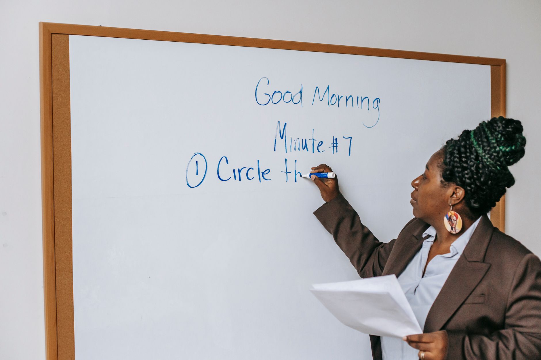 Concentrated African American female teacher in formal suit writing on whiteboard during lecture in classroom
