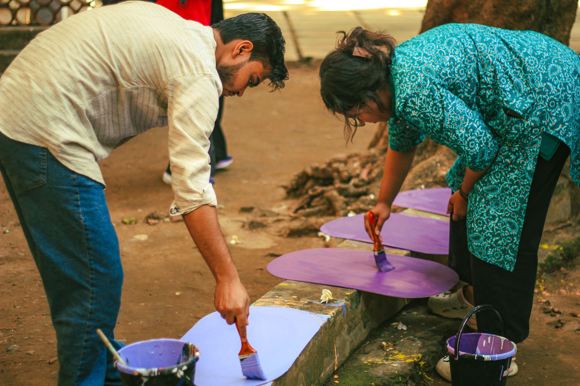 Two students painting wooden boards in vibrant colors at an outdoor art event in Dhaka, Bangladesh.