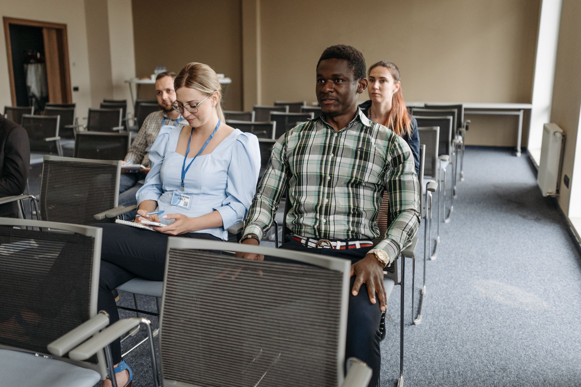 A diverse group of adults sitting in a seminar room attentively listening to a presentation.
