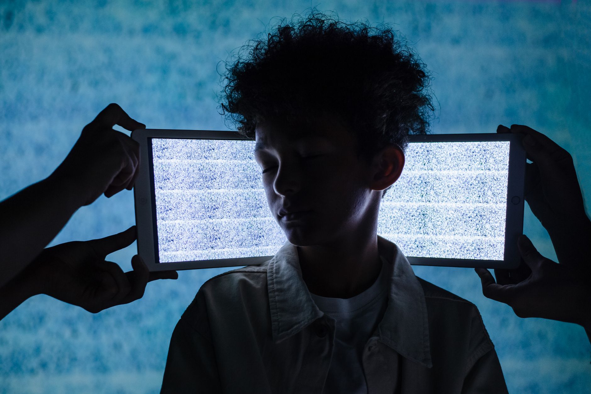 A teenager stands with eyes closed between two tablets showing digital noise, symbolizing information overload.