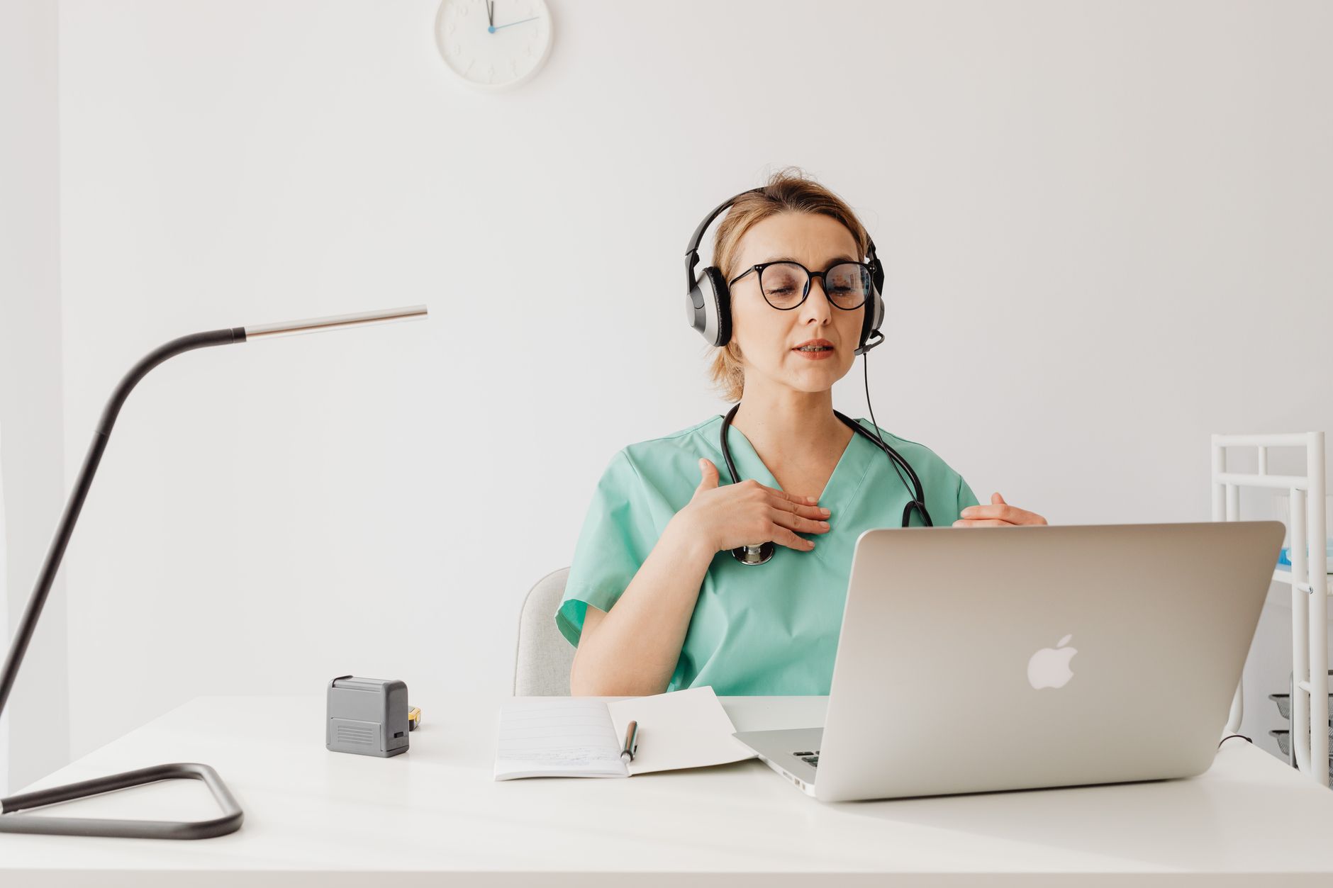 Doctor in a green scrub conducting an online video consultation using a laptop and headphones.