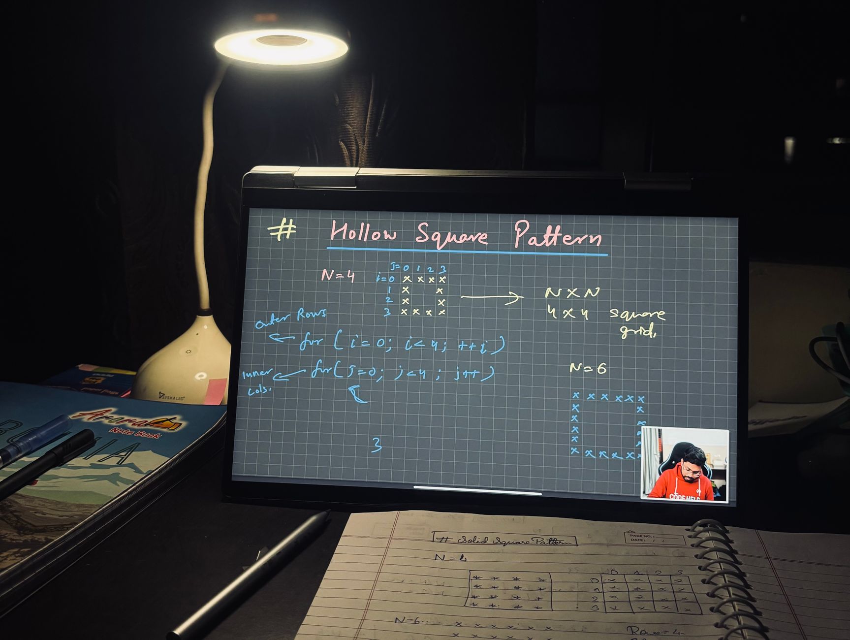 A dimly lit home study setup with laptop displaying coding notes on a hollow square pattern.