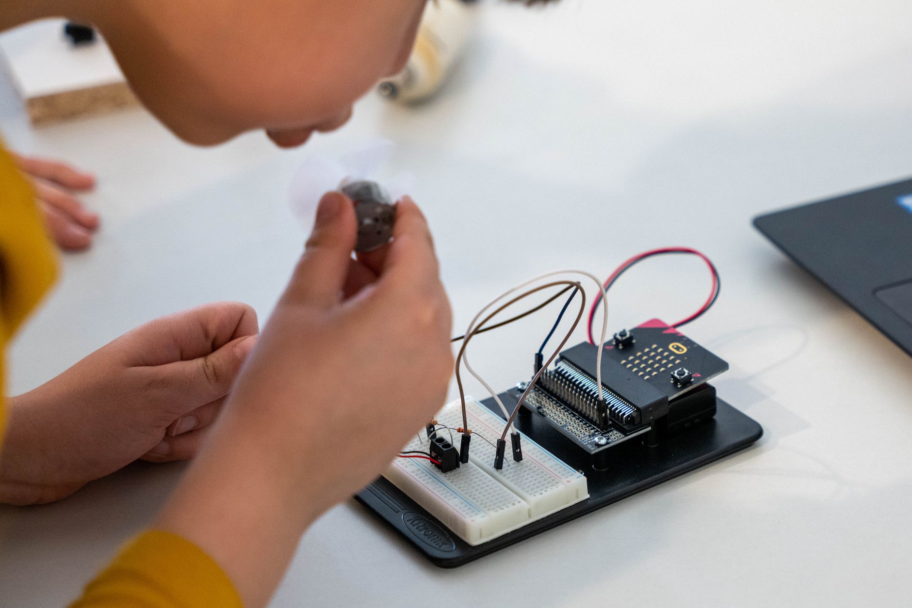 Young child assembling an electronic circuit with a microcontroller on a workbench.